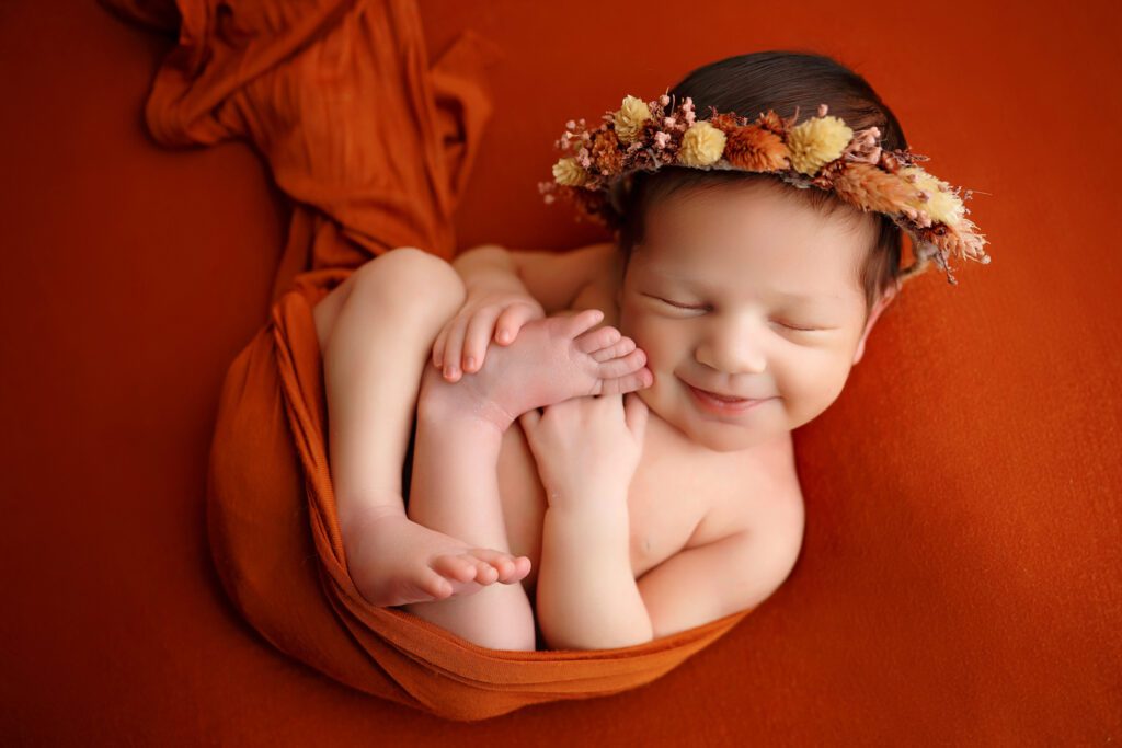 Newborn baby posed for a newborn photoshoot in a orange outfit. Baby is smiling. Sleepy newborn poses. San Antonio newborn Photographer. Best Newborn Photographer