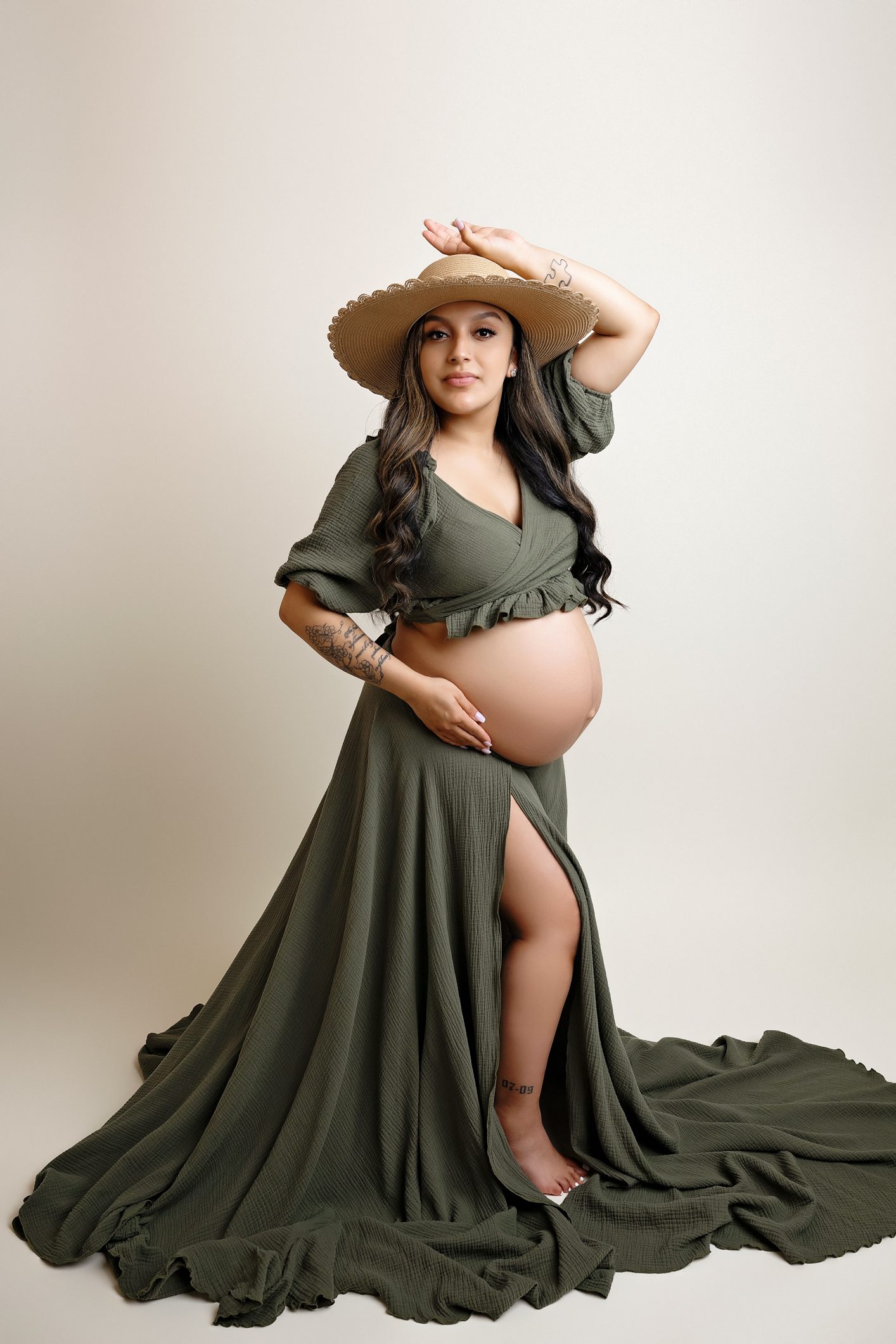 Maternity photoshoot with a cream backdrop. Green Maternity gown. Maternity shoot where mom is standing and holding her belly. San Antonio Maternity photographer. San Antonio Photographer