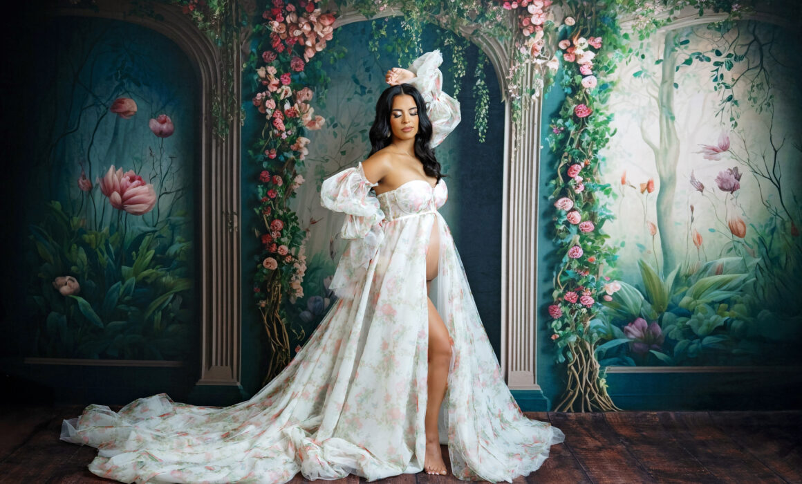 Studio maternity photoshoot in san antonio. Mom is posed with a floral backdrop and long sheer maternity gown.