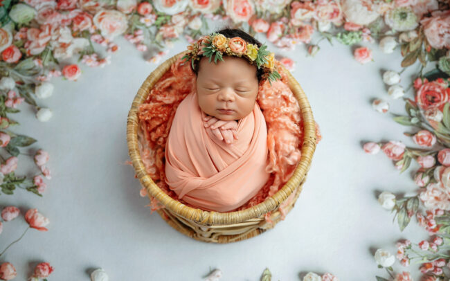 San Antonio newborn photographer poses baby girl in peach wrap surrounded by soft floral details