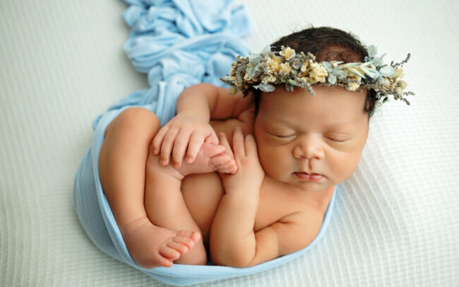 Newborn baby girl posed in a blue wrap with floral headband at San Antonio photography studio
