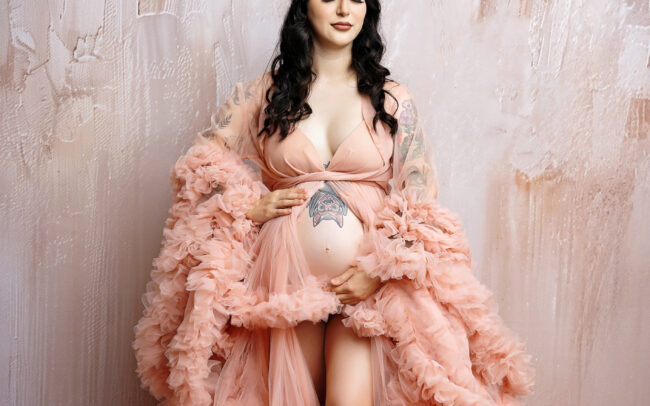 Studio maternity portrait with blush pink ruffle gown and soft backdrop