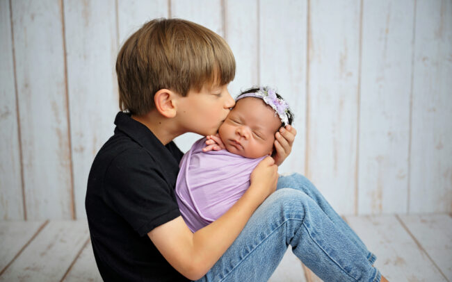 Big brother gently kissing newborn baby sister during San Antonio sibling photography session