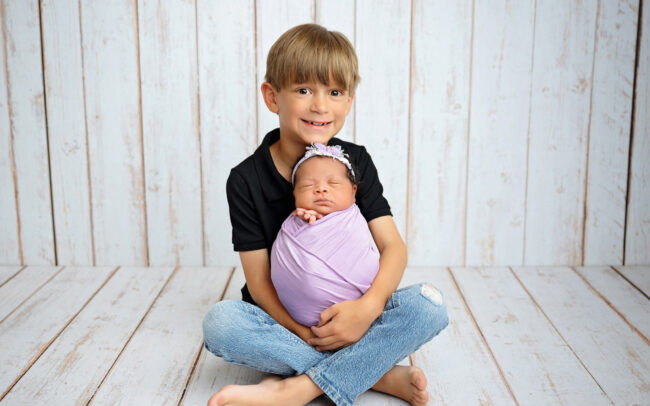 Big brother holding newborn baby sister during sibling portraits in San Antonio