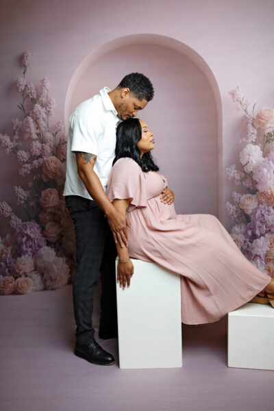 Expecting parents posing together in front of a neutral arched backdrop during their San Antonio maternity session.