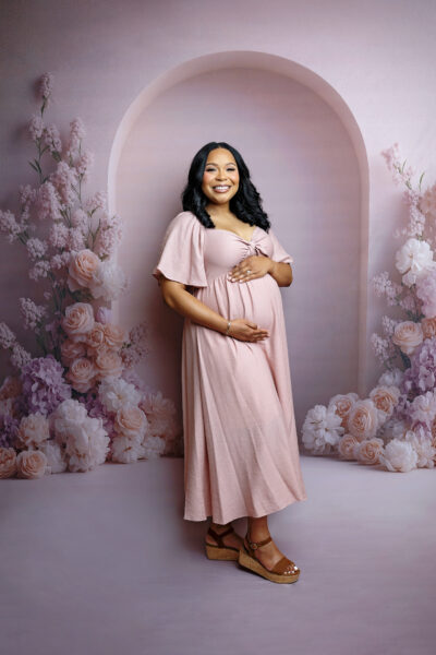 Pregnant mother wearing a blush pink dress surrounded by soft floral details during a San Antonio maternity photoshoot.