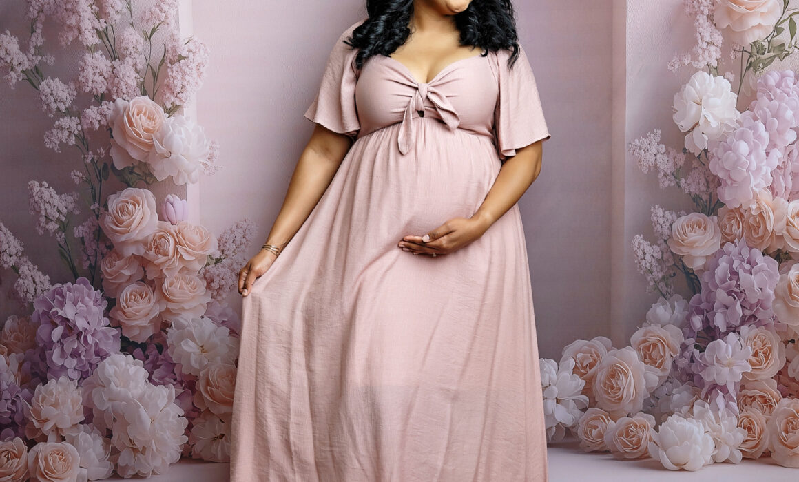 Expecting mother smiling in a flowing blush pink dress during an elegant studio maternity session in San Antonio.