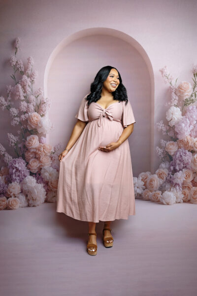 Expecting mother smiling in a flowing blush pink dress during an elegant studio maternity session in San Antonio.