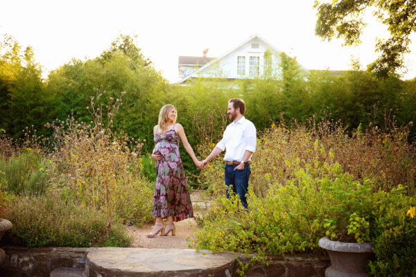Expecting couple holding hands in the gardens at Landa Library during a golden hour maternity photoshoot in San Antonio.