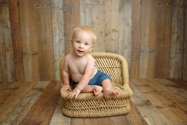 Baby sitting in a woven chair during a warm neutral milestone session in San Antonio