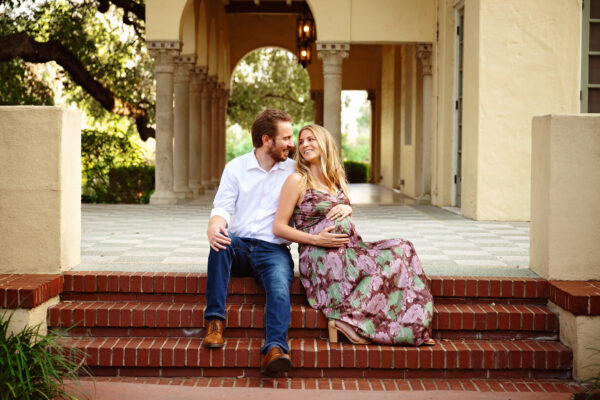 Expecting parents sitting together on brick steps during an outdoor maternity session at Landa Library in San Antonio.
