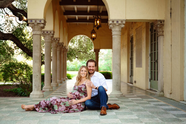 Expecting couple seated beneath the columns of Landa Library during a romantic San Antonio maternity photography session.