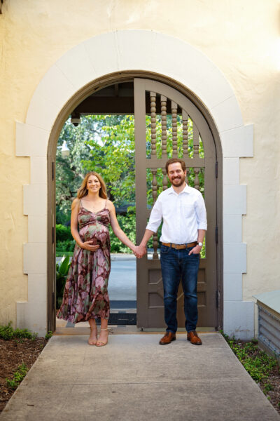 Pregnant woman and her partner holding hands beneath an arched doorway at historic Landa Library in San Antonio.