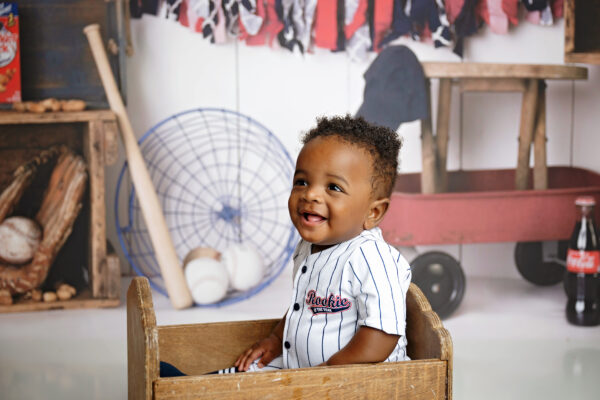 Smiling 8-month-old baby in a pinstripe baseball outfit during a studio milestone session