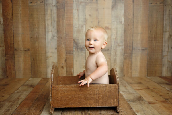 Baby standing in a rustic wooden bed during a natural milestone photography session