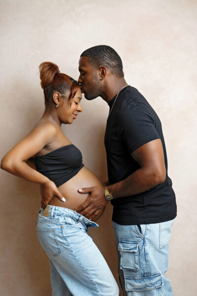 Partner kissing pregnant mother’s forehead during an intimate maternity portrait session