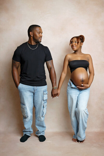 Expecting parents holding hands during a relaxed studio maternity session in San Antonio.