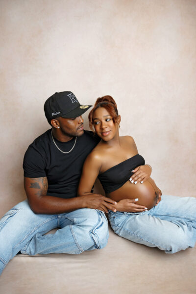 Pregnant mother and partner seated on the studio floor during a casual maternity photography session.
