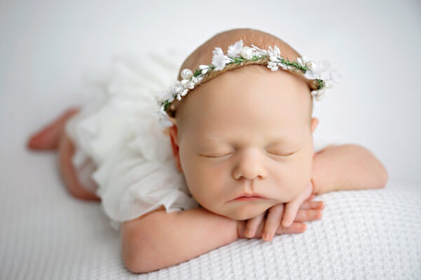 Baby girl posed in a white lace newborn outfit during her studio session