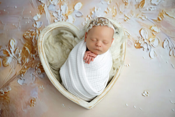 Newborn baby posed in a heart-shaped prop with soft neutral and gold styling
