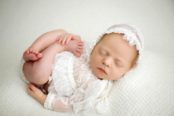 Baby girl posed in a white lace newborn outfit during her studio session