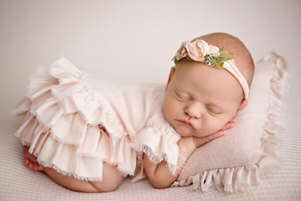Baby girl newborn portrait with delicate floral headband and soft pink styling