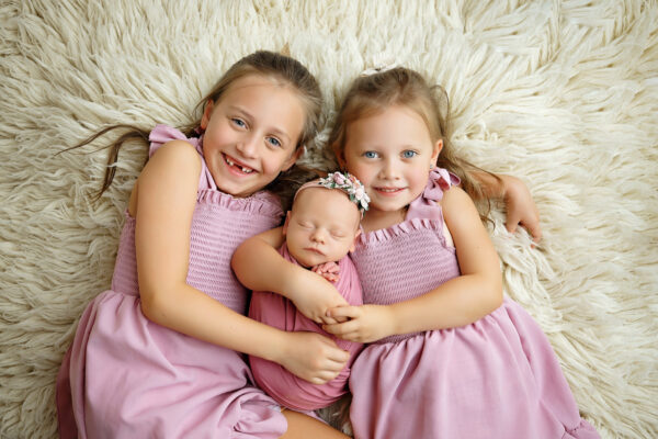 Newborn baby girl wrapped in pink with her two older sisters