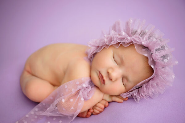 Baby girl sleeping on lavender backdrop with ruffled bonnet