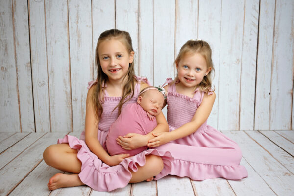 Newborn baby girl wrapped in pink with her two older sisters