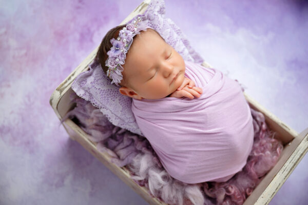 Newborn baby wrapped in lavender in vintage cream prop