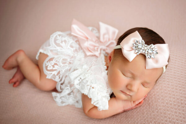 Baby girl in white lace romper with blush bow