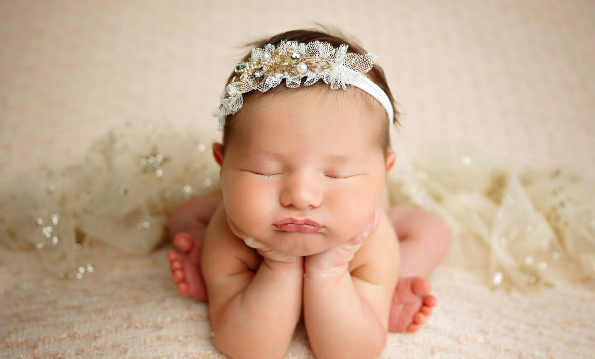 Baby girl chin-on-hands newborn pose in cream and gold