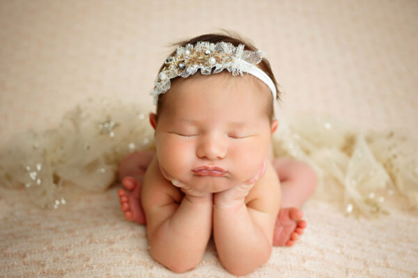 Baby girl chin-on-hands newborn pose in cream and gold