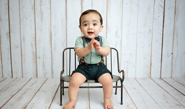 One-year-old baby boy sitting on a small chair for milestone portraits in a San Antonio photography studio