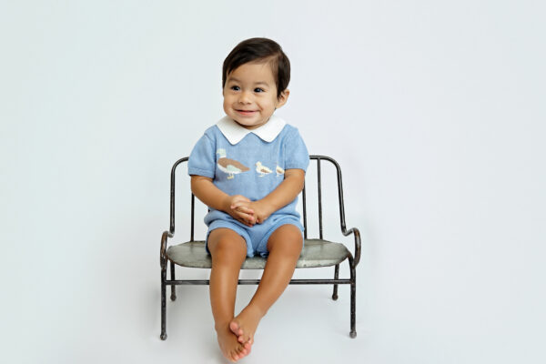 Baby boy in a blue outfit sitting on a vintage bench during his one-year milestone photos in San Antonio.