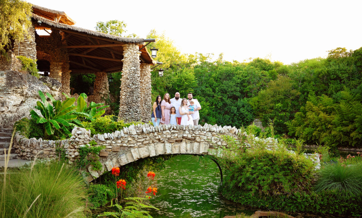 Large family posing together on a stone bridge surrounded by lush gardens in San Antonio