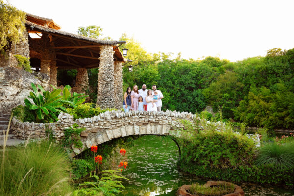 Large family posing together on a stone bridge surrounded by lush gardens in San Antonio