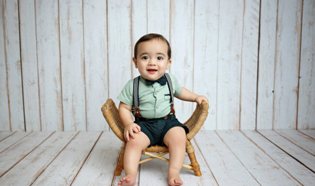 One-year-old boy sitting in a wicker chair for a simple studio birthday portrait in San Antonio