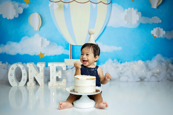 One-year-old boy laughing during a blue hot air balloon themed cake smash session in San Antonio.