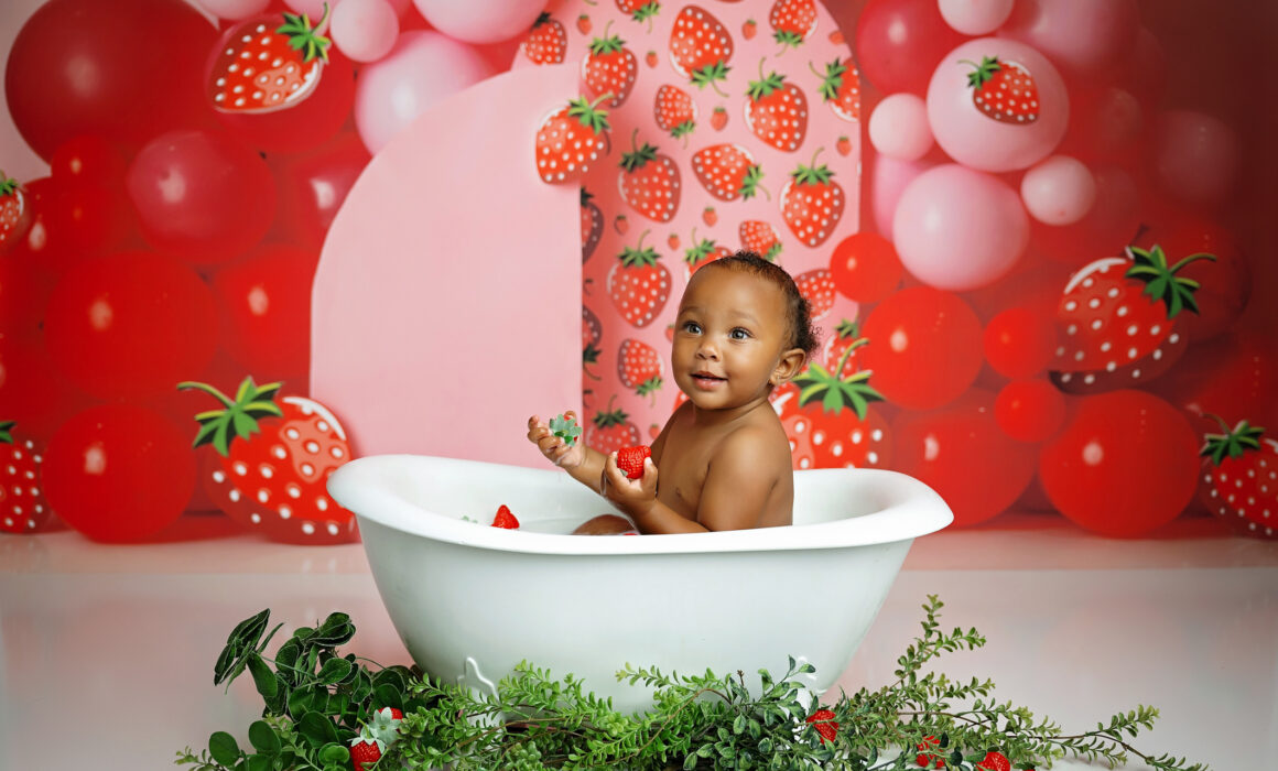 One-year-old baby enjoying a strawberry-themed birthday bath during a San Antonio first birthday photography session.
