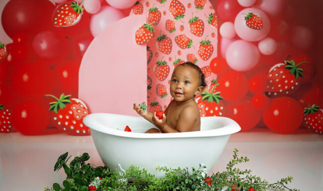 One-year-old baby enjoying a strawberry-themed birthday bath during a San Antonio first birthday photography session.