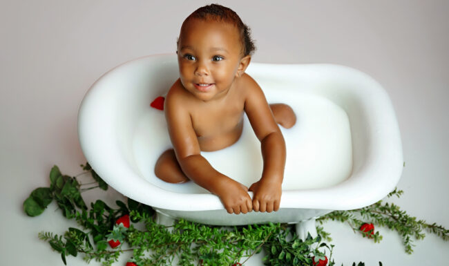 Smiling one-year-old baby sitting in a strawberry milk bath during a first birthday photo session in San Antonio.