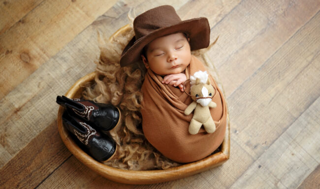 Newborn baby in a brown wrap and cowboy hat with tiny western boots during a San Antonio newborn photography session.