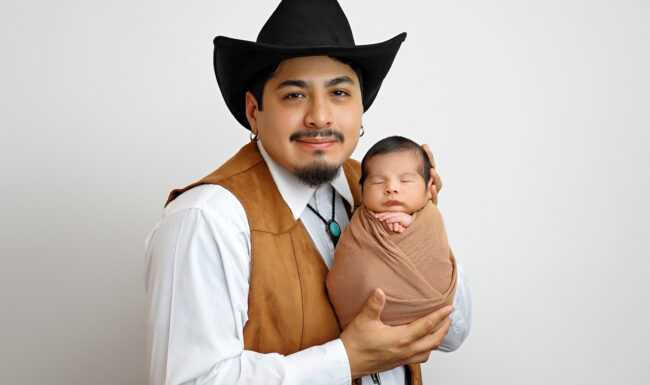 Dad wearing a cowboy hat holding his newborn baby during a studio newborn session in San Antonio, Texas.