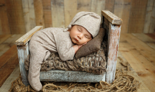 Sleeping newborn baby posed in a rustic wooden bed with neutral beige and brown textures.