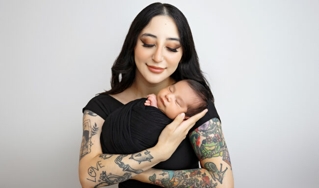 Mother smiling down at her sleeping newborn during a timeless studio newborn portrait in San Antonio.
