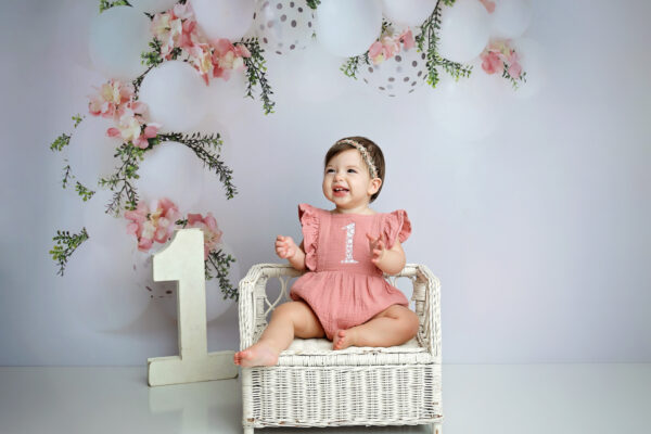 One-year-old girl smiling during a pink floral first birthday photography session in San Antonio
