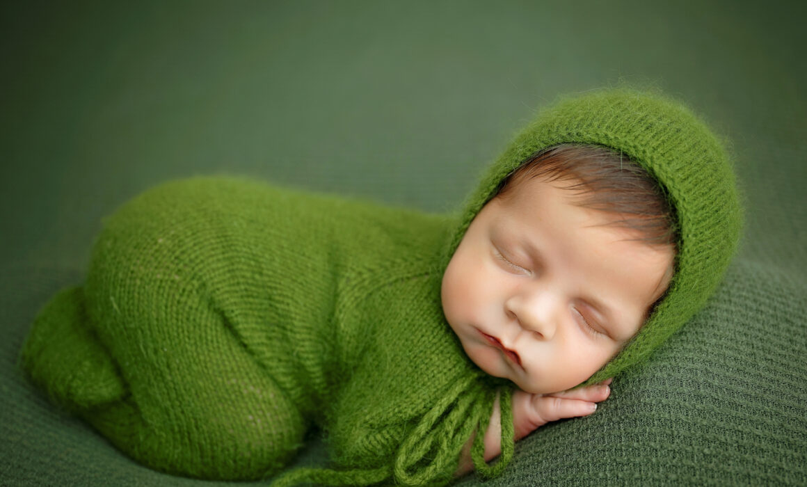 Sleeping baby boy in a green bonnet during a posed newborn photography session in San Antonio.