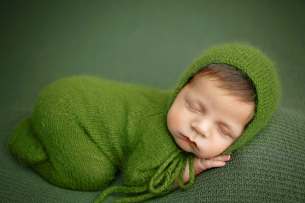 Sleeping baby boy in a green bonnet during a posed newborn photography session in San Antonio.