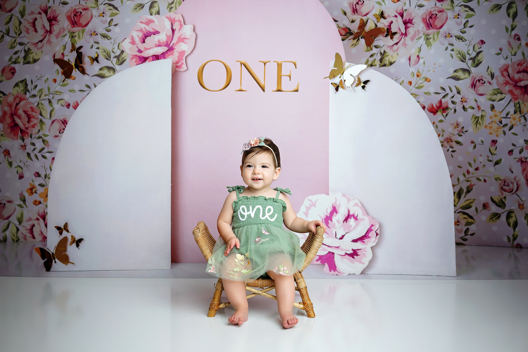 One-year-old girl in a sage green dress photographed on a pink floral garden birthday backdrop